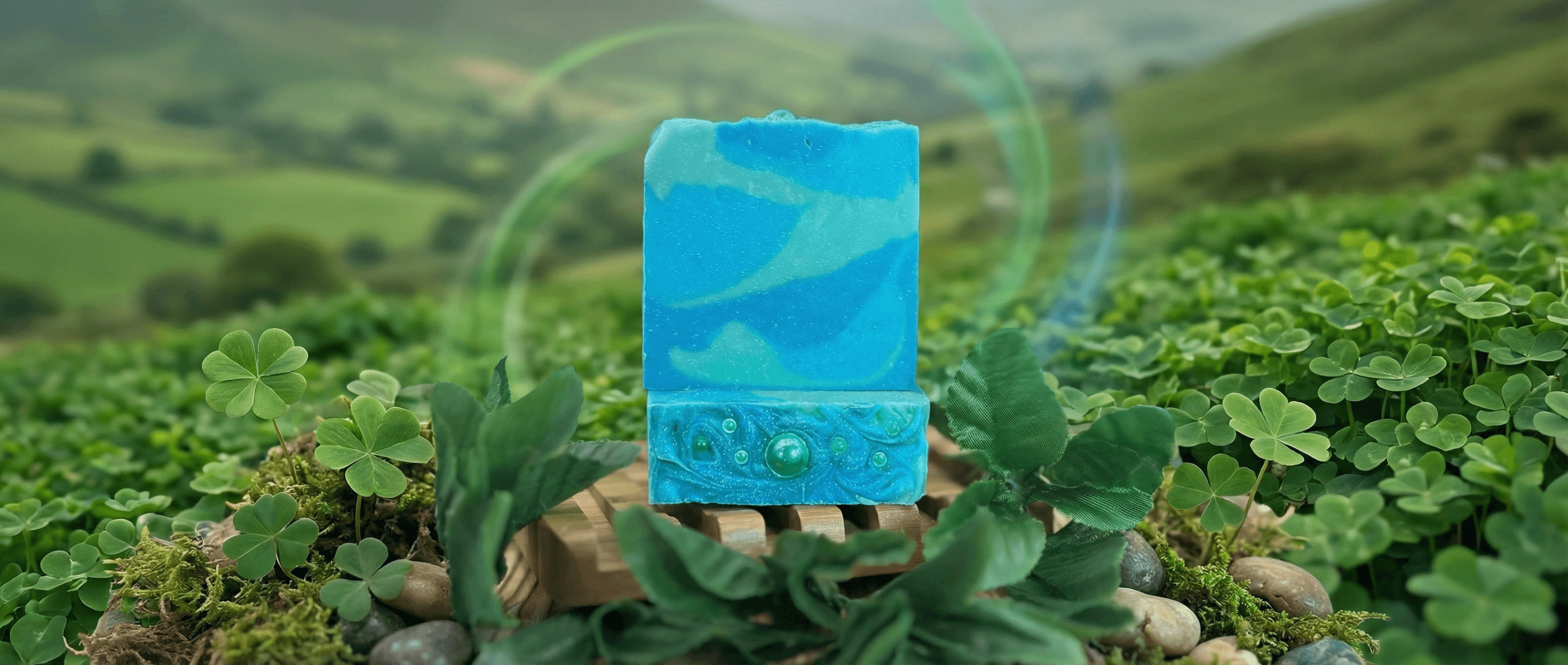 Vibrant blue handmade soap bar with swirled marbling and embedded bubbles, displayed on wooden soap dish surrounded by clover leaves and moss in outdoor garden setting.