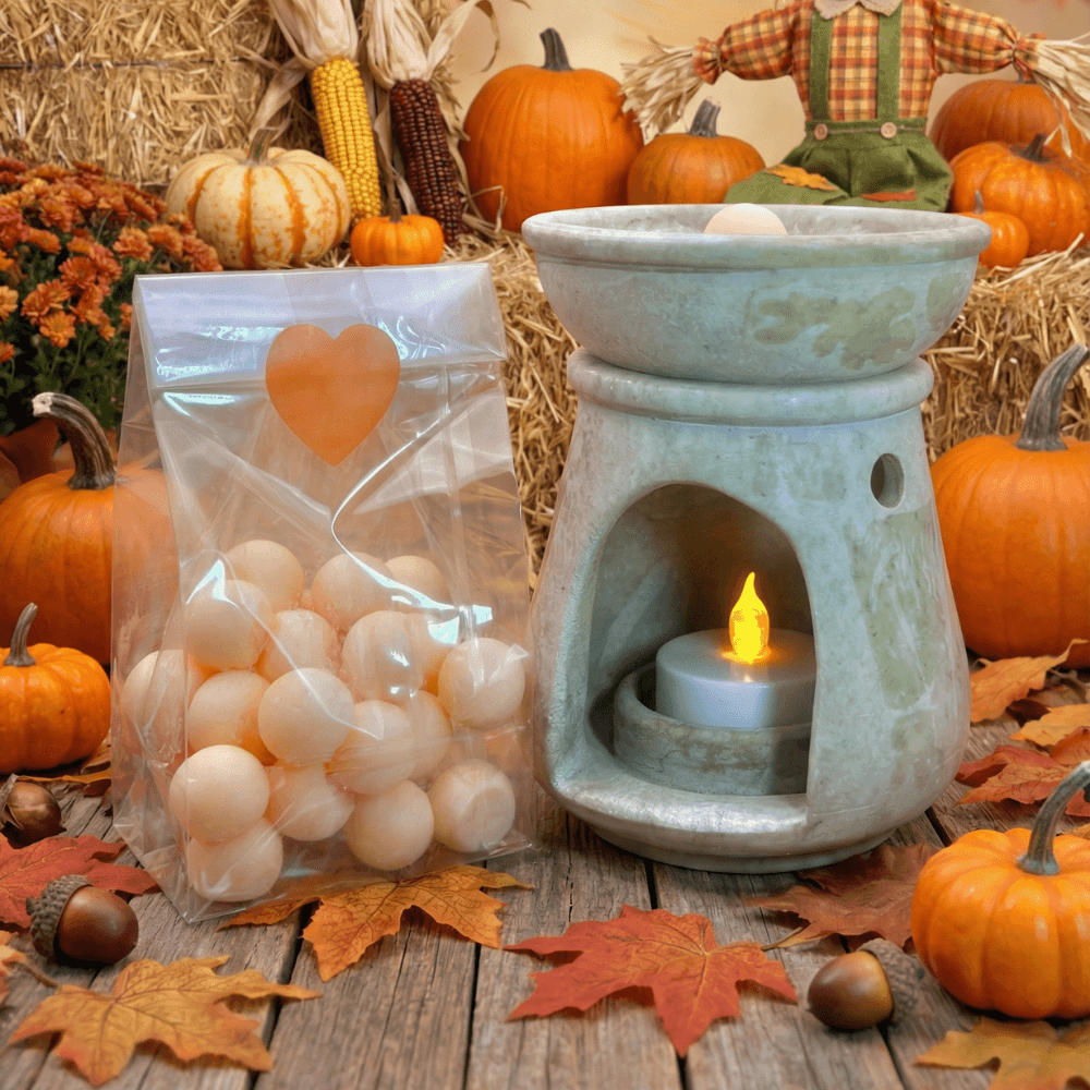Clear bag of ivory-colored wax melt spheres beside a turquoise ceramic wax warmer with flickering LED candle, styled with autumn pumpkins, corn, hay bales, and fall leaves.