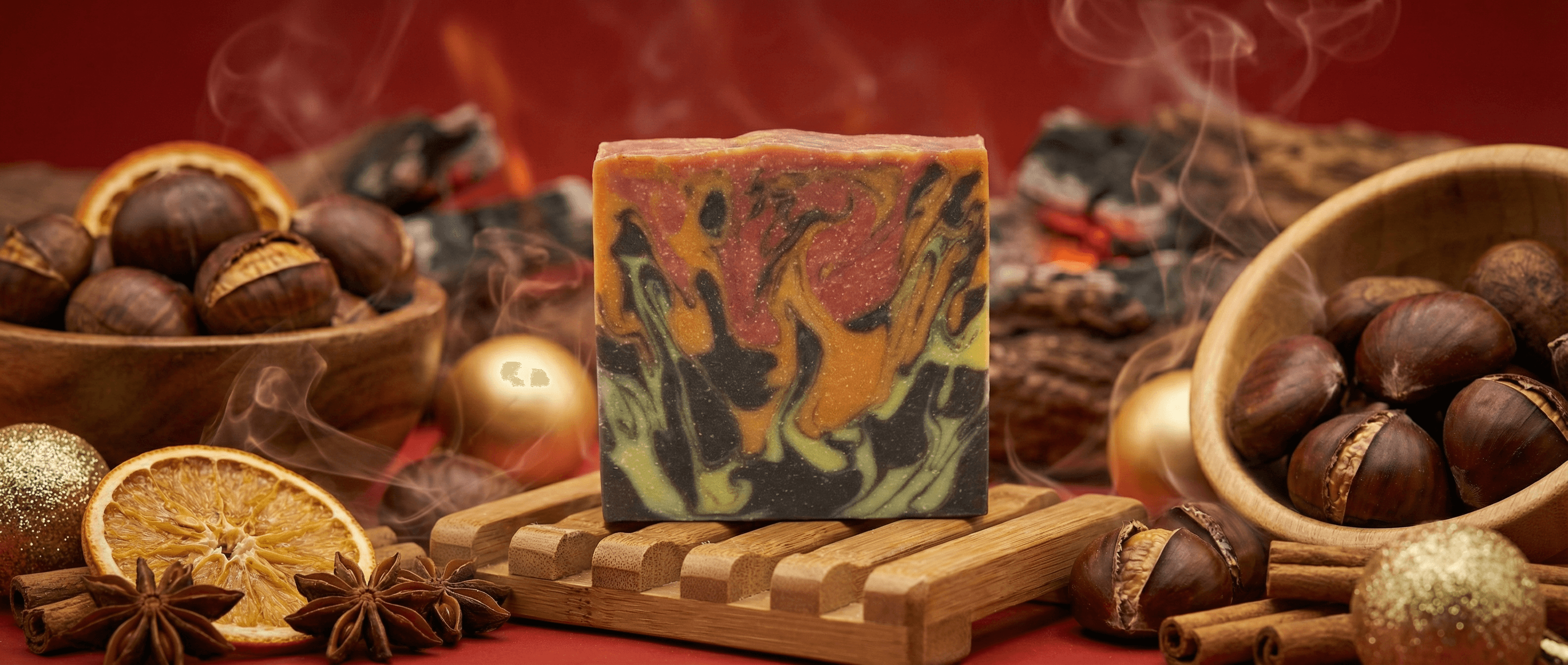 Handcrafted soap bar with dramatic fire-colored swirls in orange, red, green, and black, displayed on a wooden soap dish surrounded by roasted chestnuts, dried orange slices, star anise, and cinnamon sticks with warm glowing embers in the background.