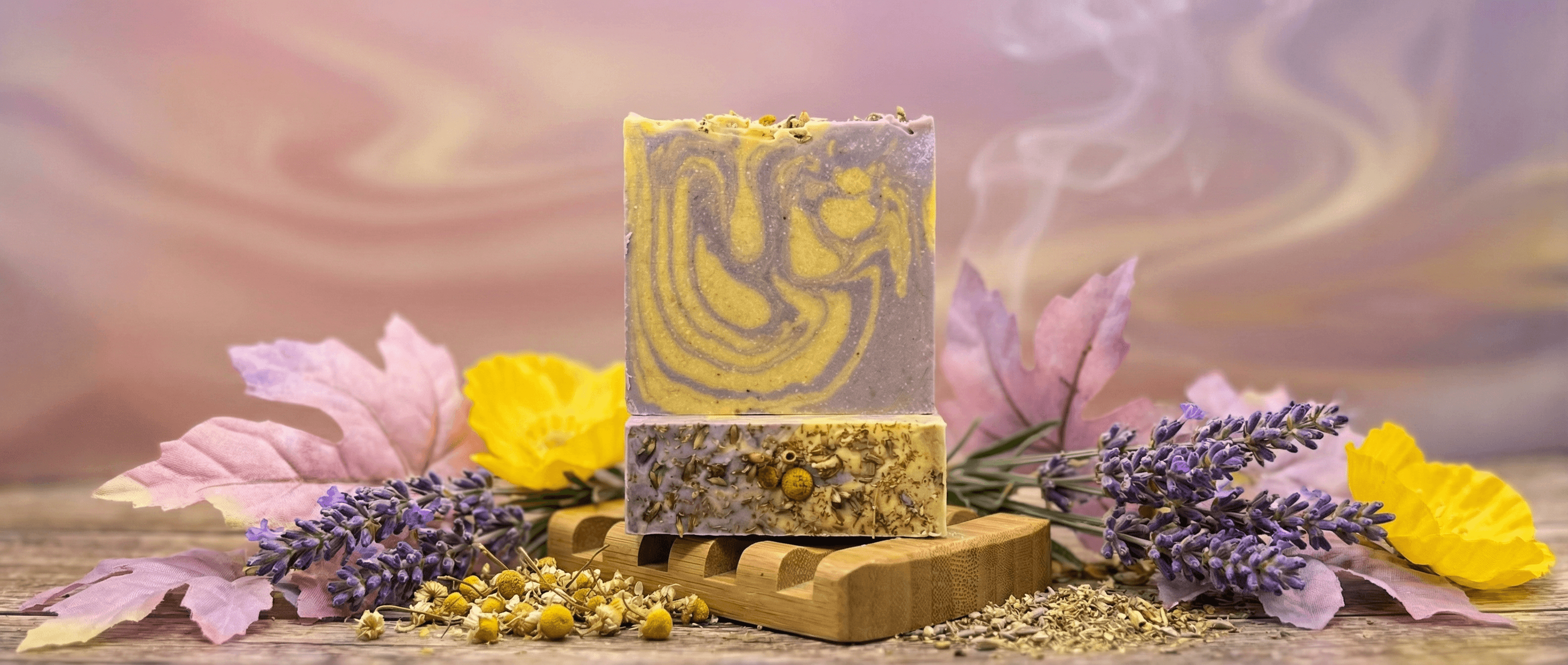 Handcrafted bar soap with purple-gray and yellow marbled swirls on top, speckled chamomile-embedded base, displayed on wooden soap dish with lavender sprigs and dried flowers.