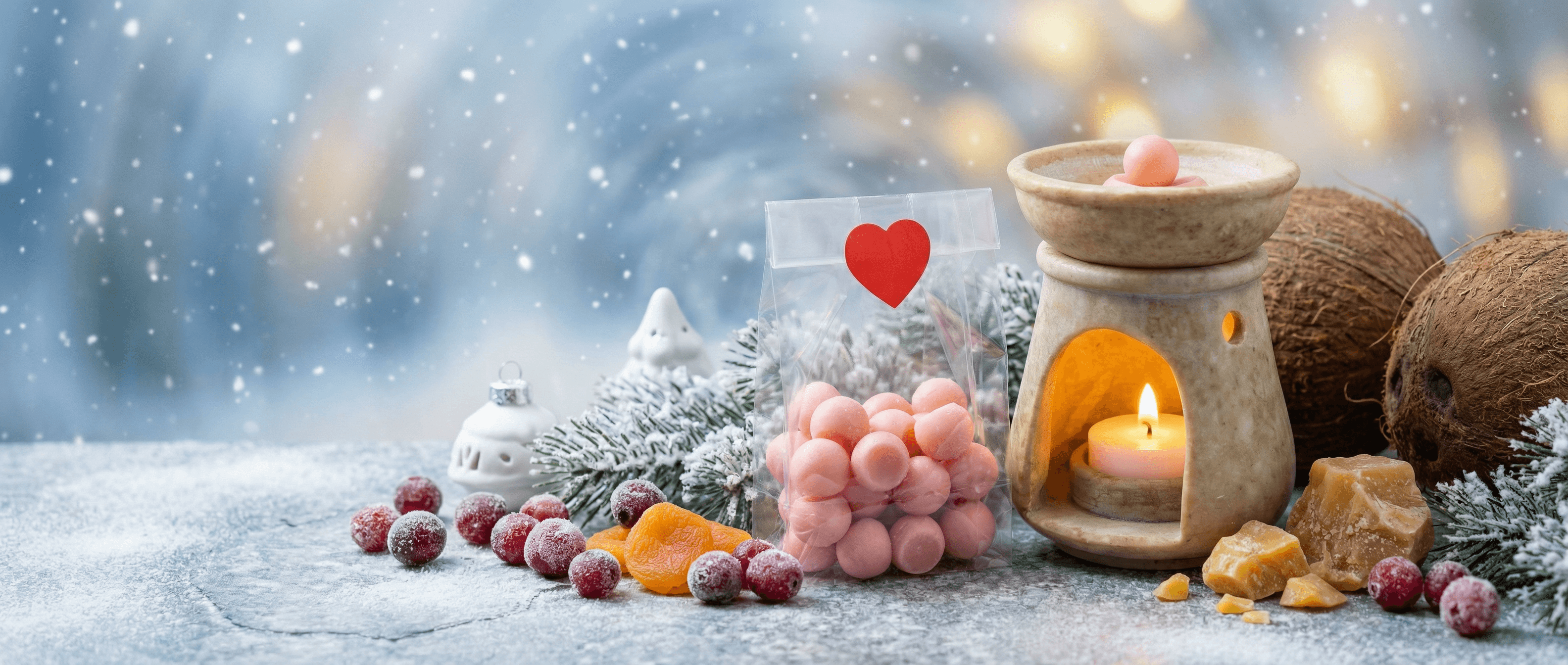 Pink bubble-shaped wax melts in clear bag with red heart, beside stone oil warmer with lit candle, frosted cranberries, coconut, and snowy pine branches in winter scene.