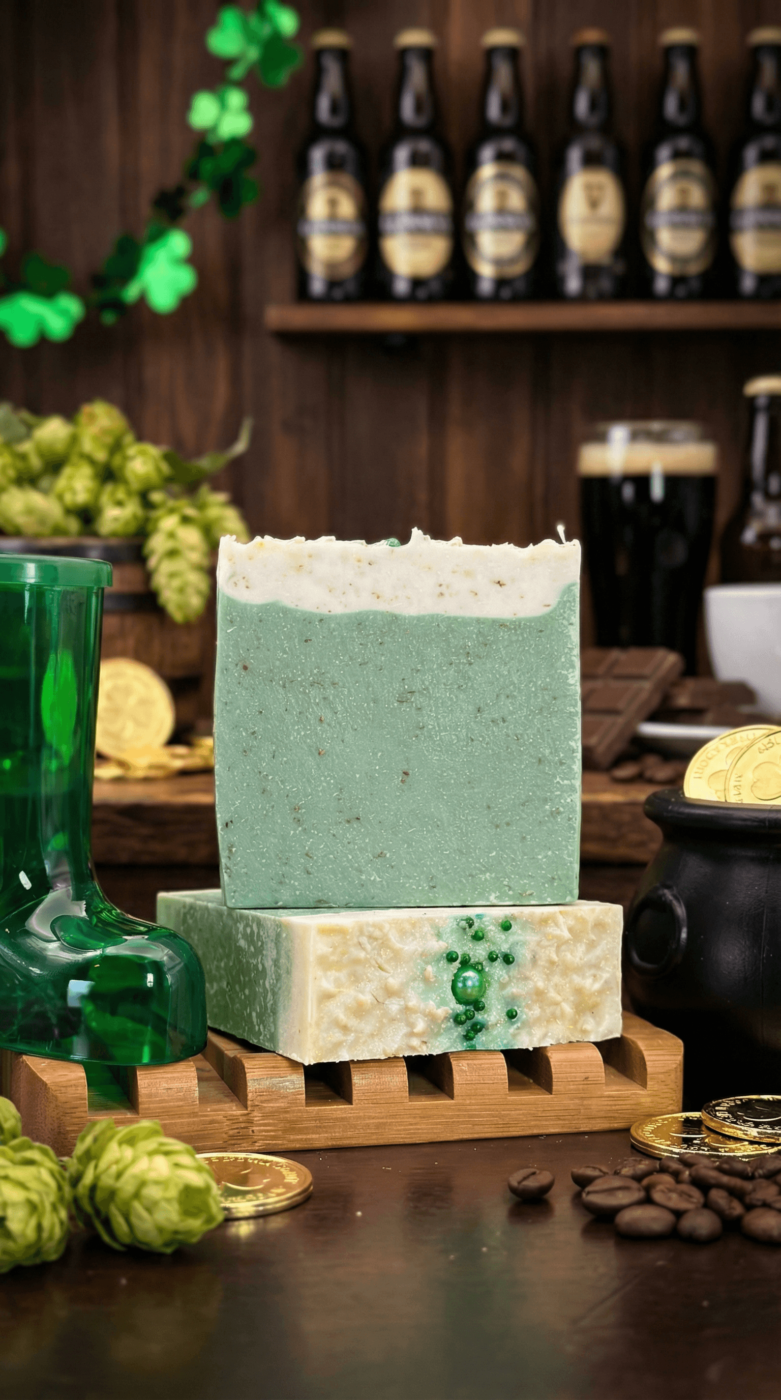 Two bars of handmade soap stacked on a wooden soap dish. The top bar is mint green with cream-colored top; the bottom bar is ivory with green shamrock embeds and specks.